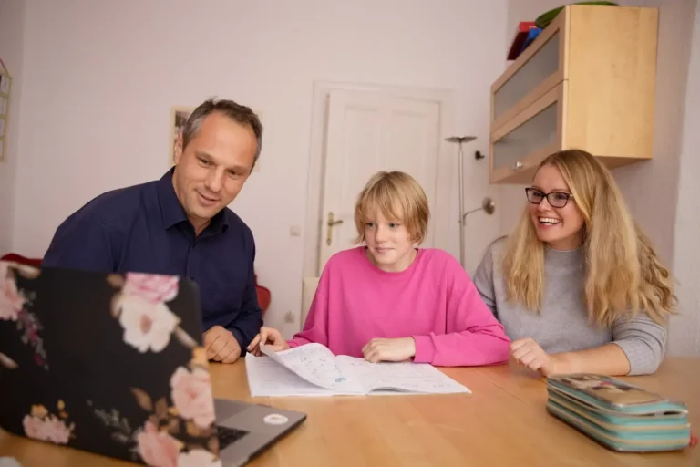 Father and mother sitting with their teenage son at the kitchen table, helping him with homework