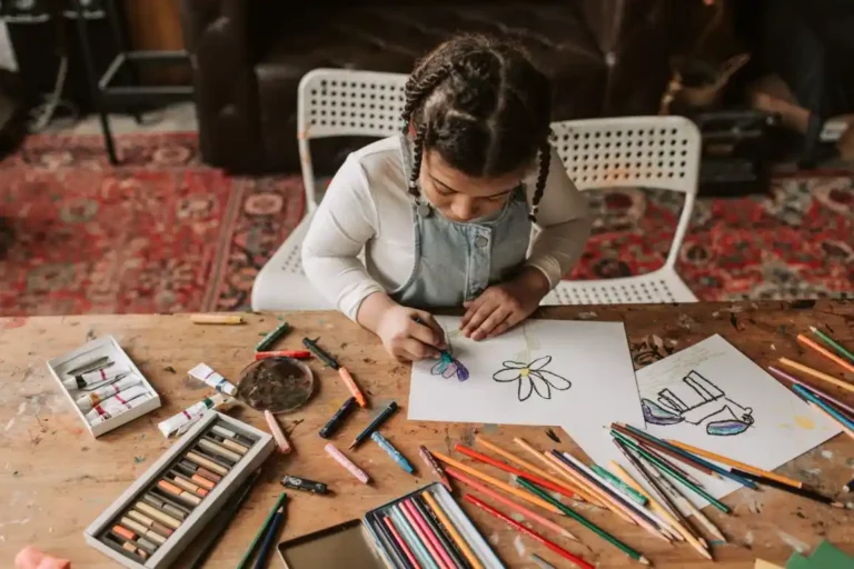 Young girl with braided hair concentrating on a drawing activity, surrounded by colored pencils and crayons on a wooden table