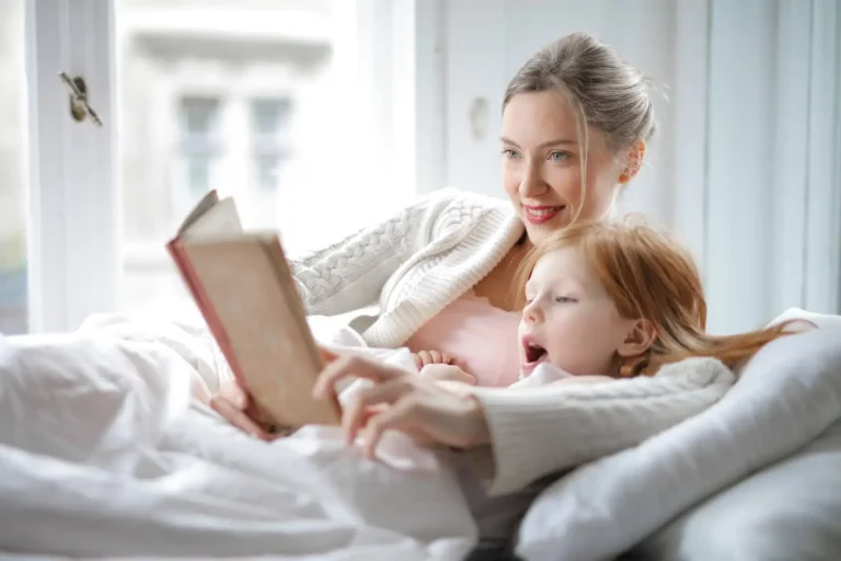 Smiling mother lying in bed reading a picture book together with her young child, cozy morning moment