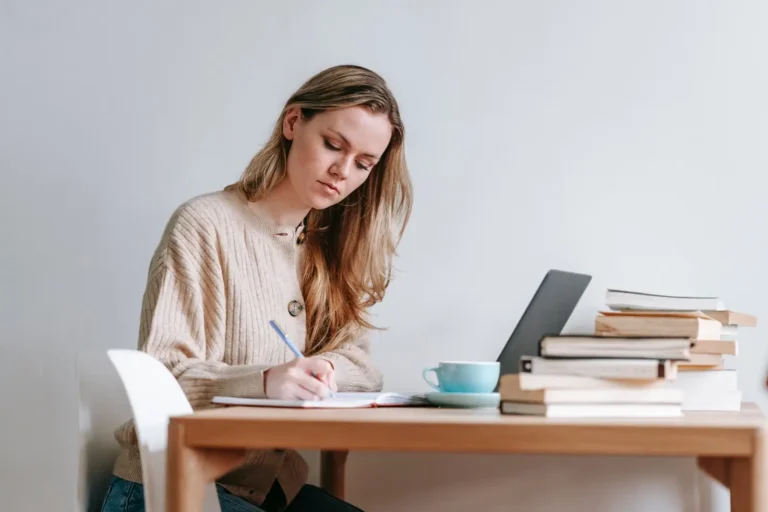 Parent sitting at a home desk, writing thoughtful notes surrounded by books and a warm cup of coffee