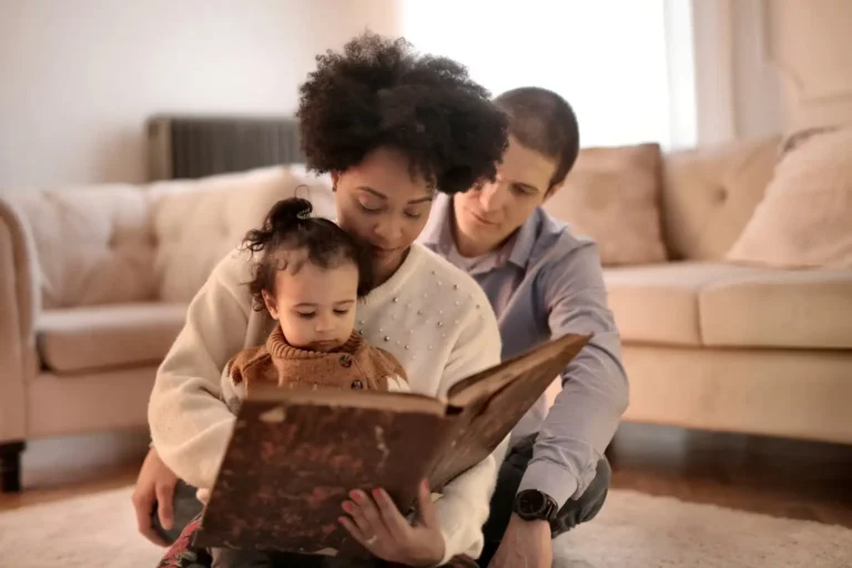 Mother and father sitting together on a sofa, reading a picture book with their toddler, modeling engaged parenting