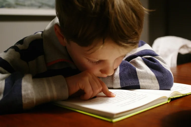 Young child reading a book independently at a wooden table, representing early literacy development