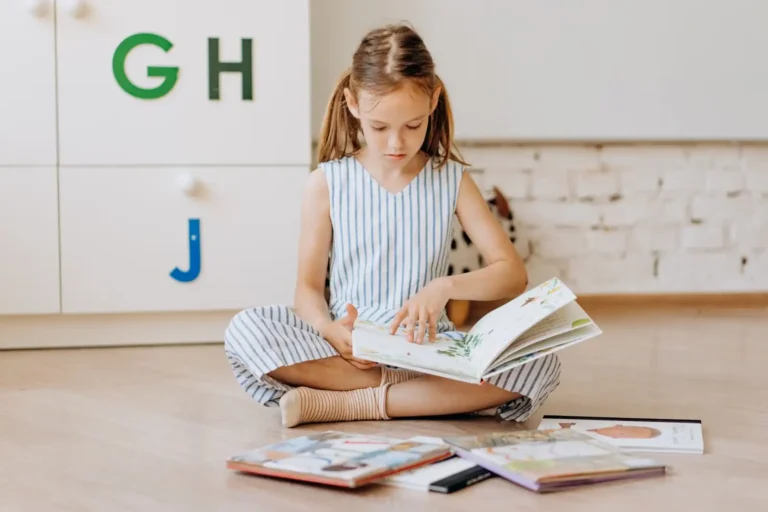 Young girl sitting cross-legged on the floor with several picture books open around her, exploring reading at her own pace